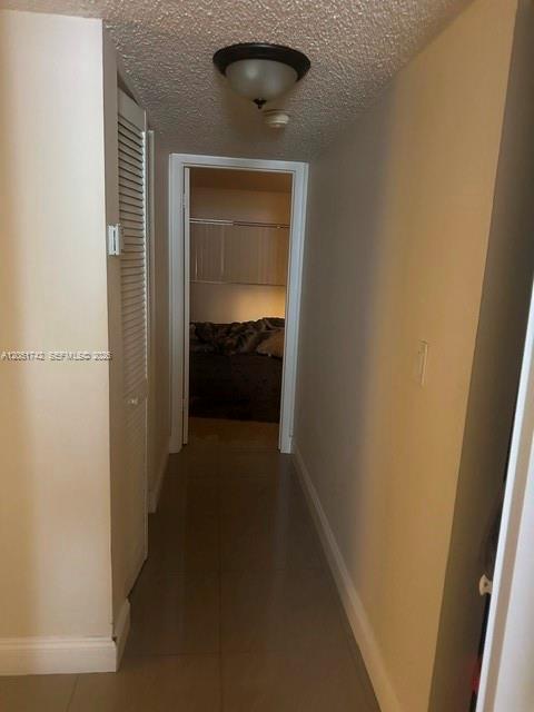 A hallway with light-colored walls and tile flooring leads to a bedroom doorway — MIAMI, FL