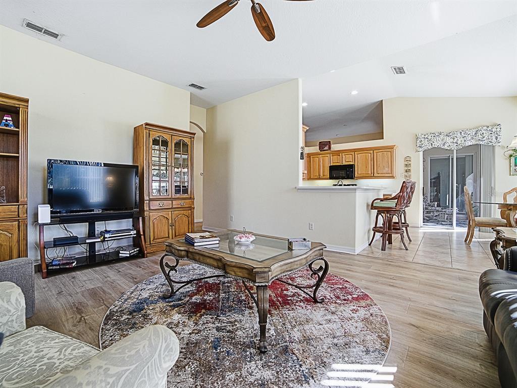 A living room with a glass coffee table, circular rug, and an open kitchen beyond — 24239 BELLE MEDE DRIVE, LEESBURG, FL
