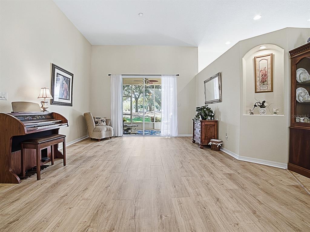 A living area with wood-look tile flooring, a piano, and sliding glass doors to a patio — 24239 BELLE MEDE DRIVE, LEESBURG, FL