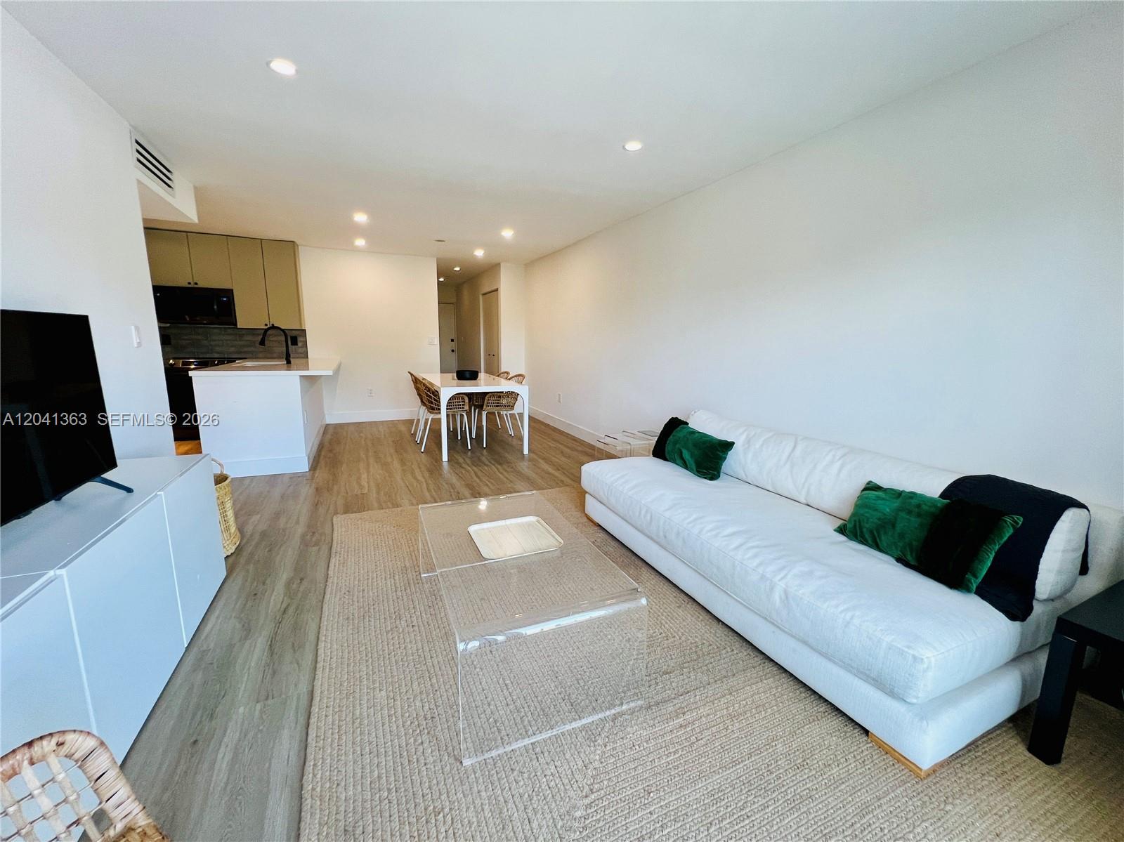 A living room with a white sofa, glass coffee table, and an adjacent kitchen area — 1900 Meridian Ave # 306, Miami Beach FL 33139, MIAMI BEACH, FL