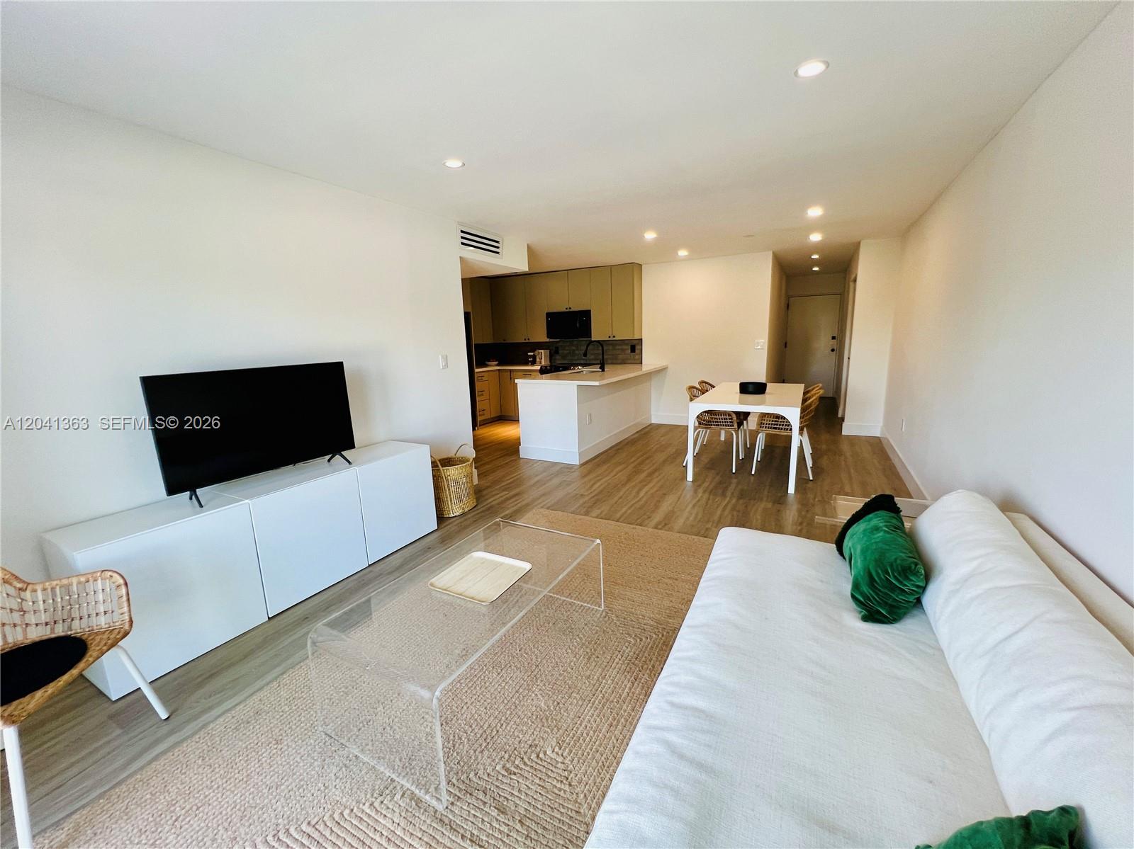 A living room and kitchen area with light wood floors, white furniture, and a dining table — 1900 Meridian Ave # 306, Miami Beach FL 33139, MIAMI BEACH, FL