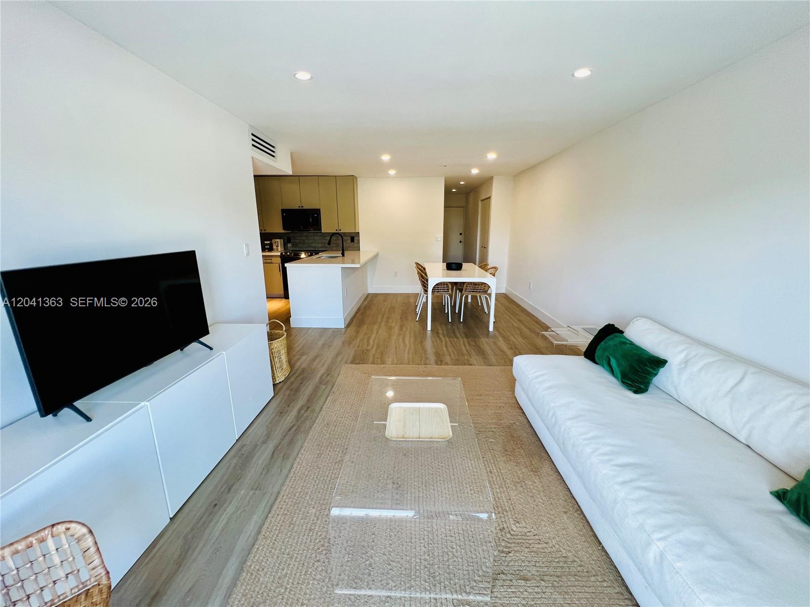 An open-concept living and dining area features light wood floors, white walls, and modern furniture — 1900 Meridian Ave # 306, Miami Beach FL 33139, MIAMI BEACH, FL