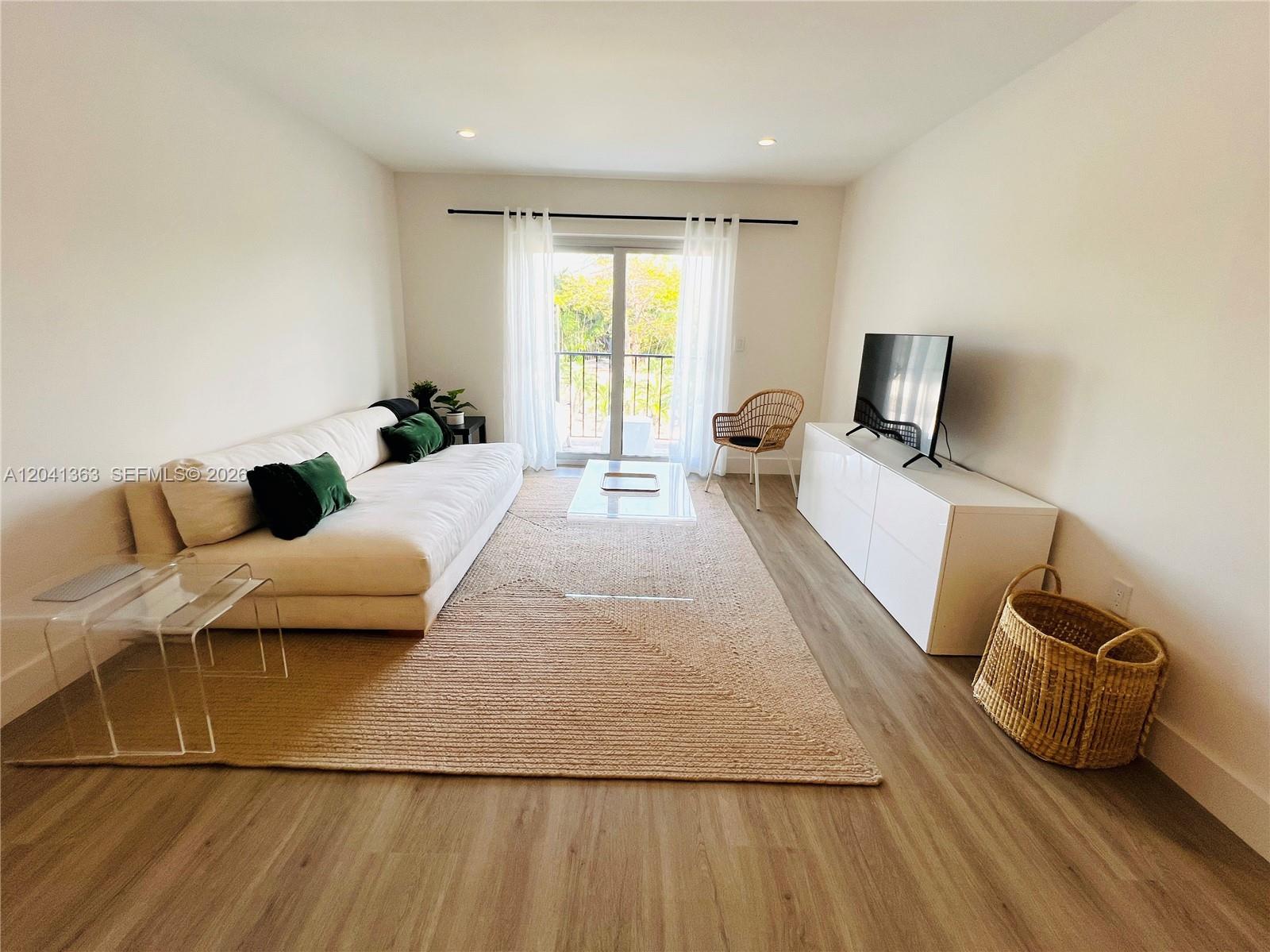 A living room features a white sofa, a glass coffee table, and wood-look flooring — 1900 Meridian Ave # 306, Miami Beach FL 33139, MIAMI BEACH, FL