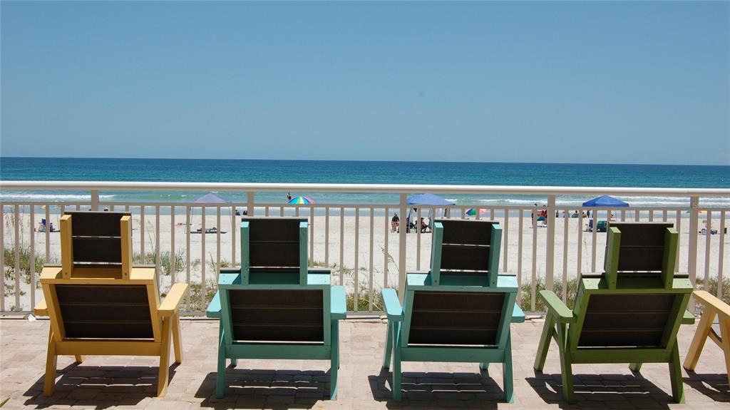 Four colorful chairs sit on a paved patio overlooking a sandy beach and the ocean — 4453 S ATLANTIC AVENUE UNIT 604, PONCE INLET, FL