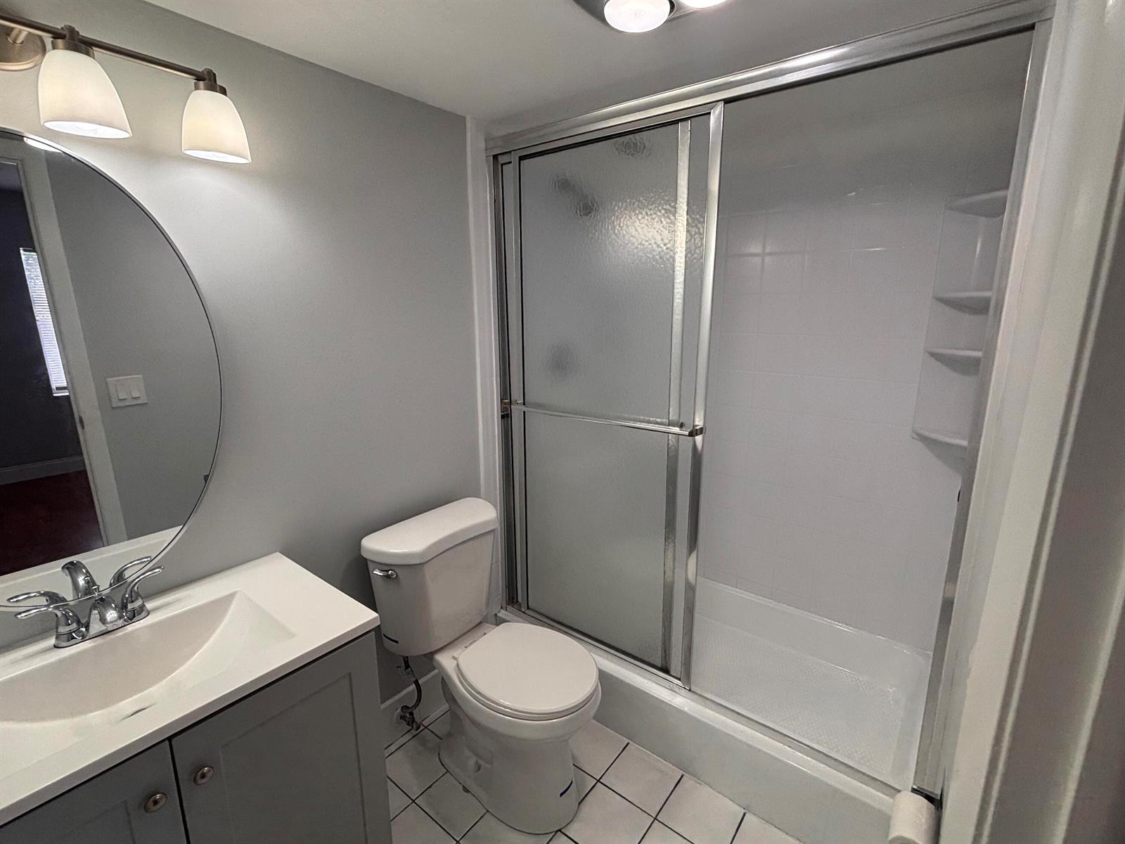 A bathroom features a gray vanity, a round mirror, a toilet, and a glass-enclosed shower — 6100 S Falls Circle Drive # 204, Lauderhill FL 33319, LAUDERHILL, FL