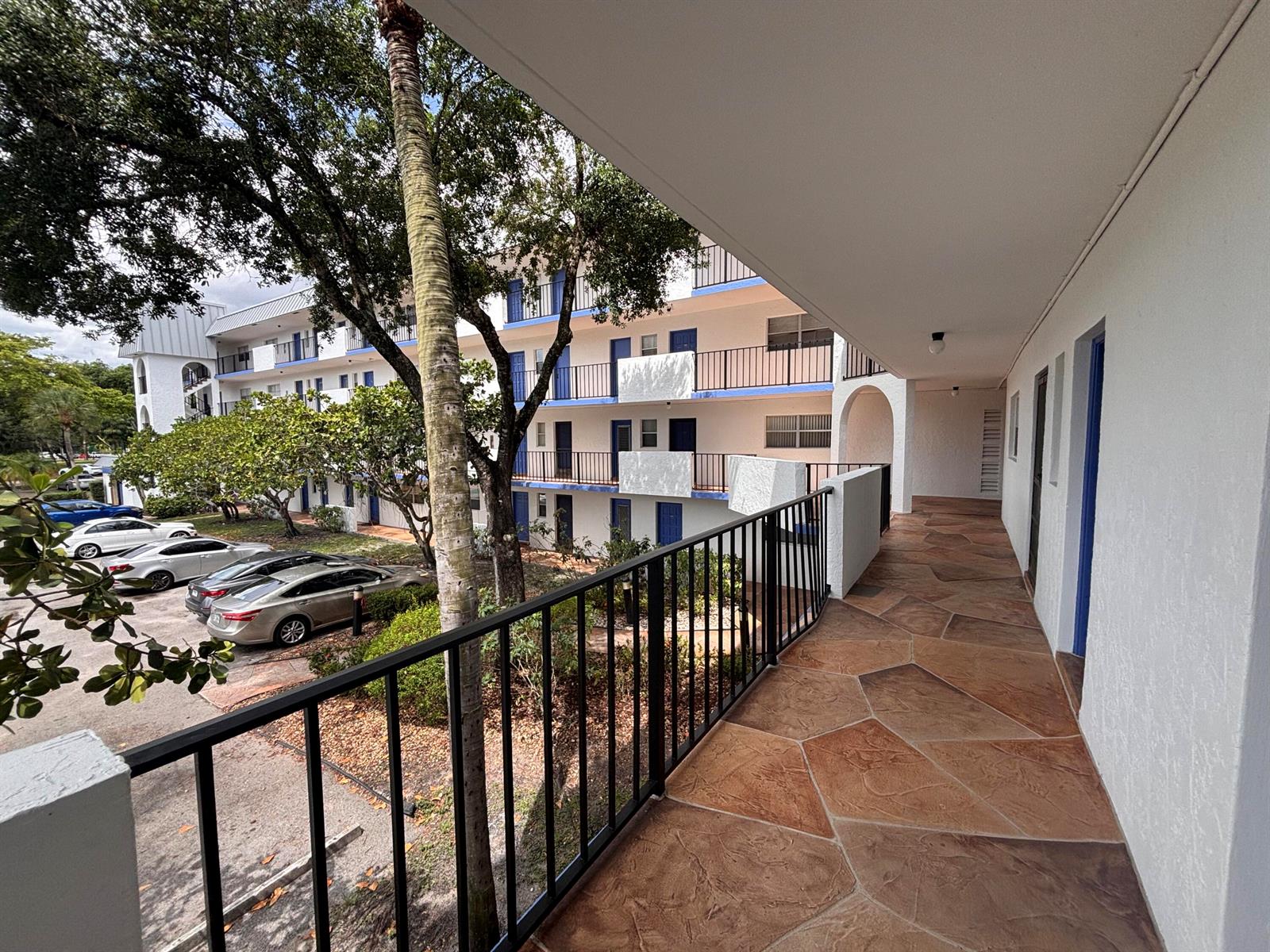 An outdoor walkway with stone-patterned flooring overlooks a parking lot and apartment building exterior — 6100 S Falls Circle Drive # 204, Lauderhill FL 33319, LAUDERHILL, FL