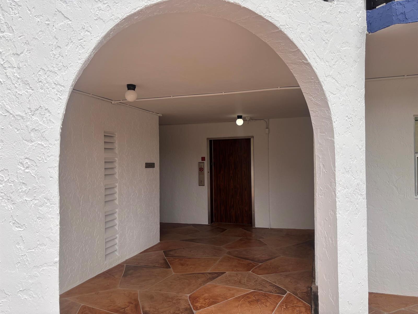 A covered entryway features a white arched opening, tiled flooring, and a wooden elevator door — 6100 S Falls Circle Drive # 204, Lauderhill FL 33319, LAUDERHILL, FL