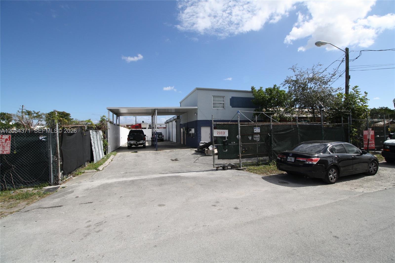 A fenced commercial property features a paved lot, a covered parking area, and a building — 2103 SW 59th Ter, West Park FL 33023, WEST PARK, FL