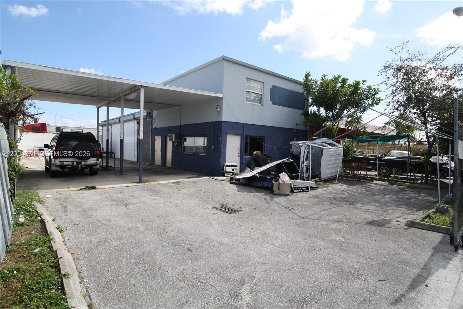 A two-story commercial building features a large metal carport and an adjacent paved parking area — 2103 SW 59th Ter, West Park FL 33023, WEST PARK, FL