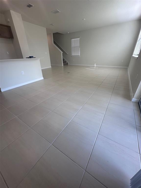 An open-concept living area features light-colored tile flooring, a kitchen island, and a staircase — 17539 SAW PALMETTO AVENUE, CLERMONT, FL