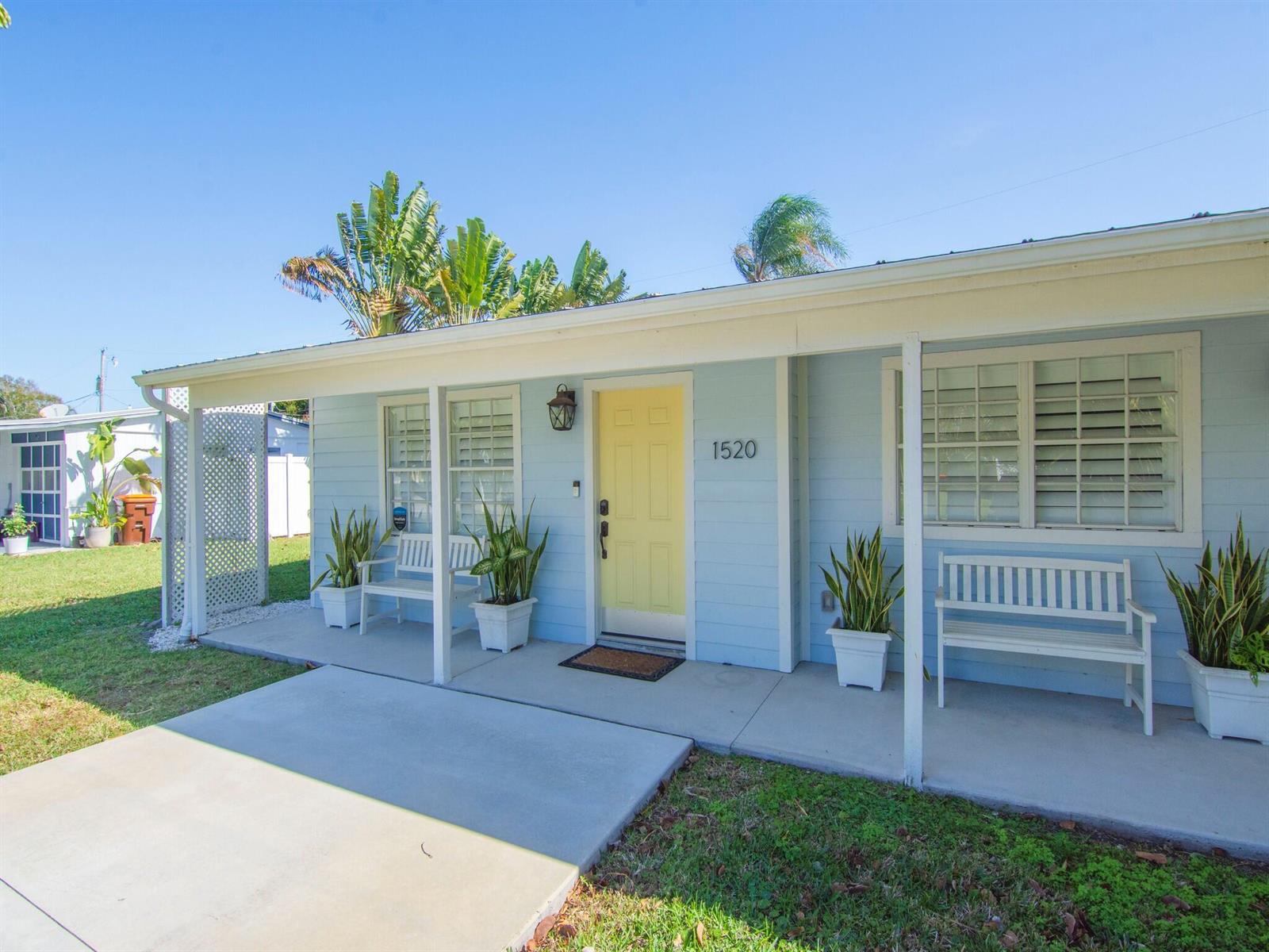A light blue house features a yellow front door, a covered porch, and white benches — VERO BEACH, FL