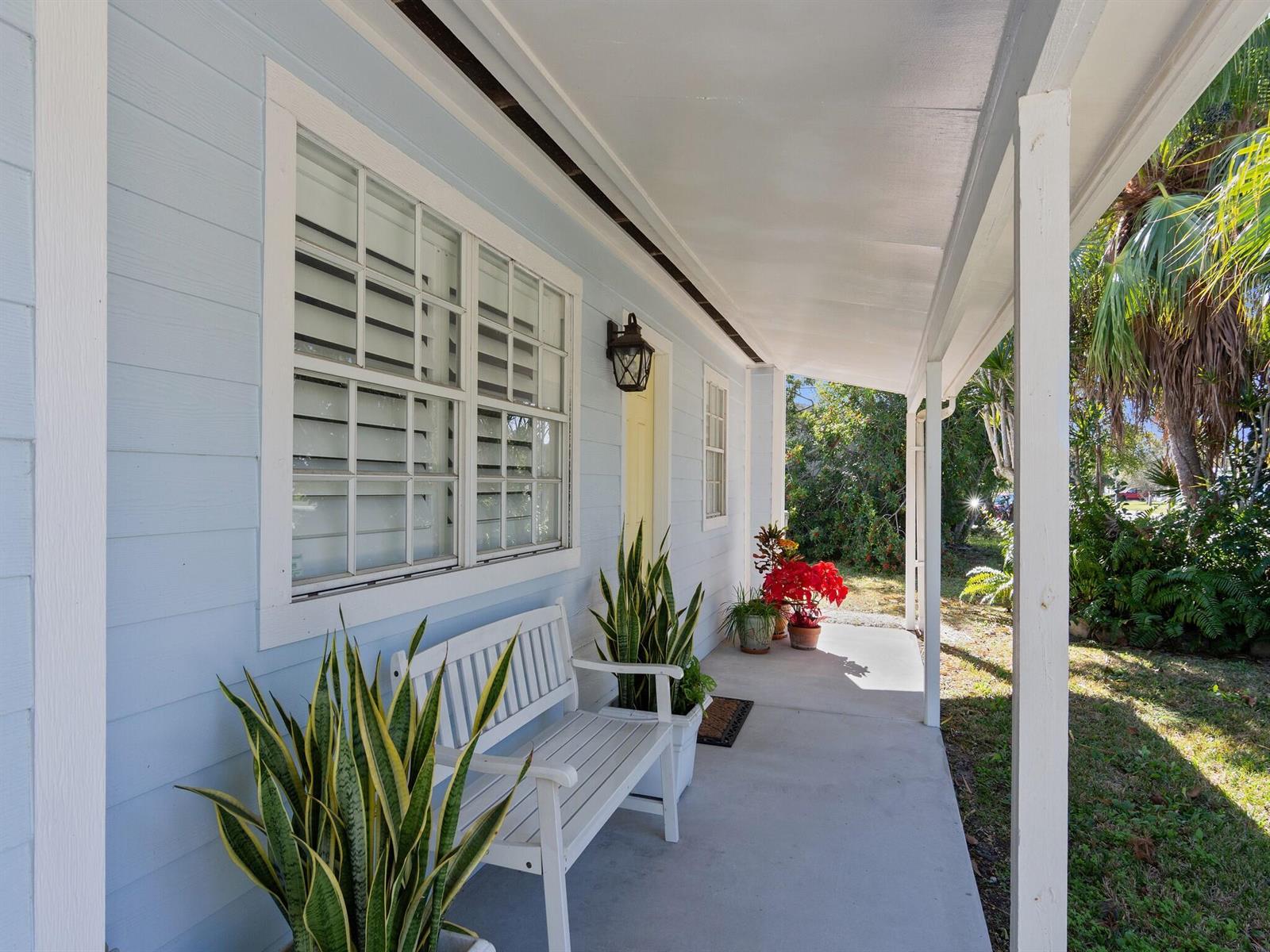 A light blue house features a covered front porch with a white bench and plants — VERO BEACH, FL