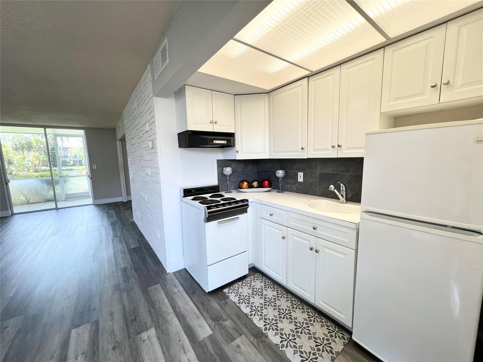 A kitchen features white cabinets, a white stove, a refrigerator, and a patterned floor mat — 777 SE 2nd Avenue # A102, Deerfield Beach FL 33441, DEERFIELD BEACH, FL