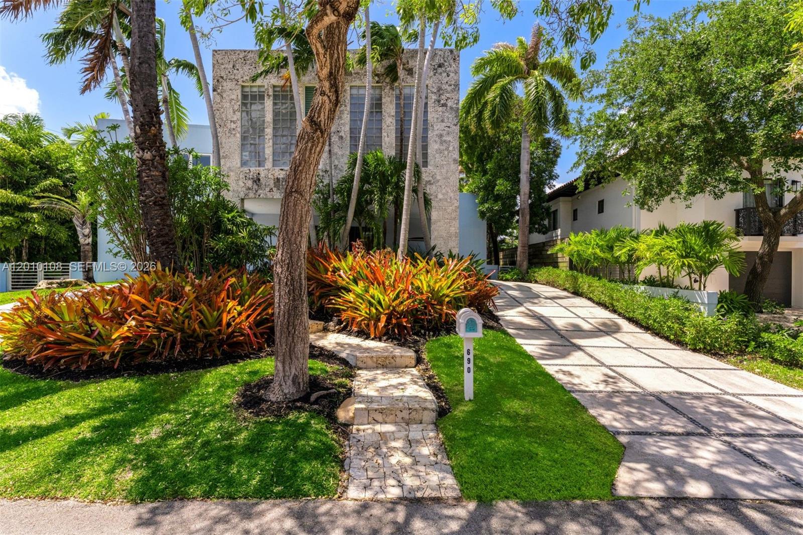 A stone-faced house features a paved driveway, a landscaped front yard, and a stone walkway — 690 Warren Ln, Key Biscayne FL 33149, KEY BISCAYNE, FL