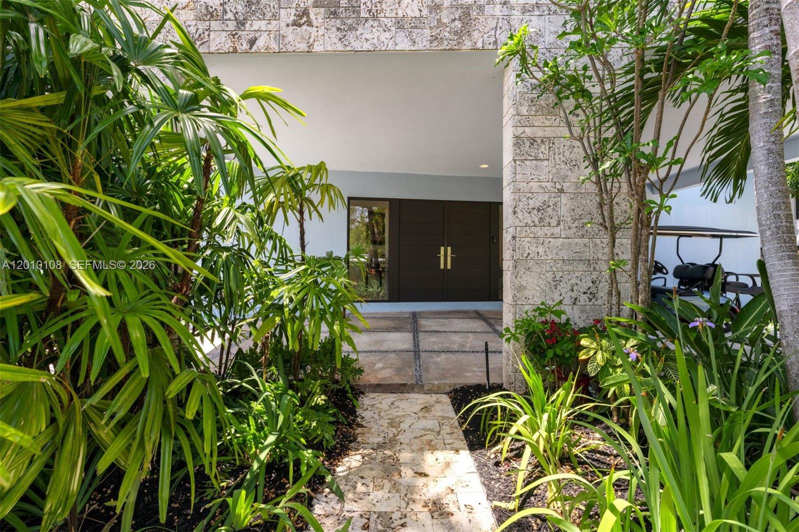 A stone walkway leads through lush tropical landscaping to a modern home entrance with double doors — 690 Warren Ln, Key Biscayne FL 33149, KEY BISCAYNE, FL