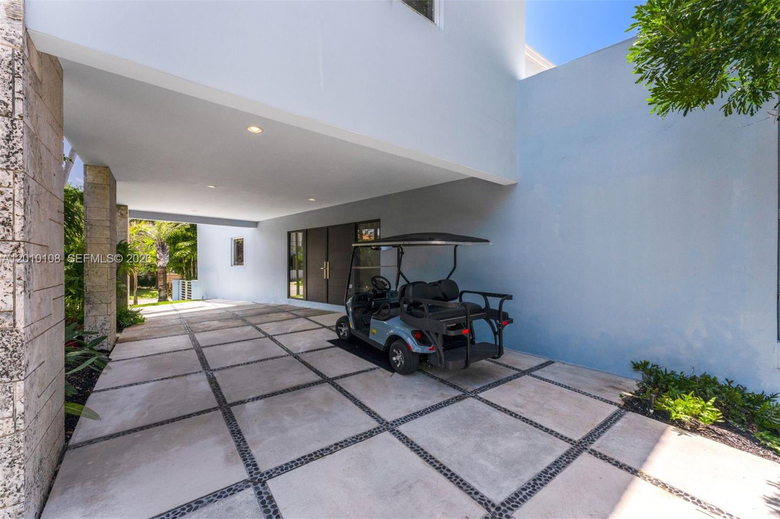 A golf cart is parked on a paved driveway under a modern house overhang — 690 Warren Ln, Key Biscayne FL 33149, KEY BISCAYNE, FL