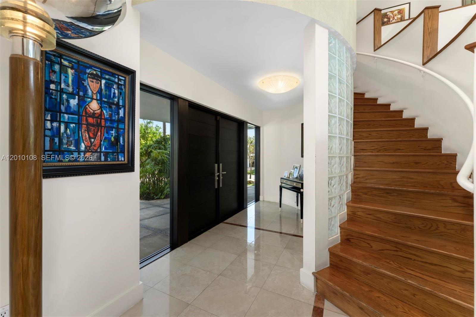 An entryway features a curved staircase, glass block wall, tile flooring, and dark double doors — 690 Warren Ln, Key Biscayne FL 33149, KEY BISCAYNE, FL