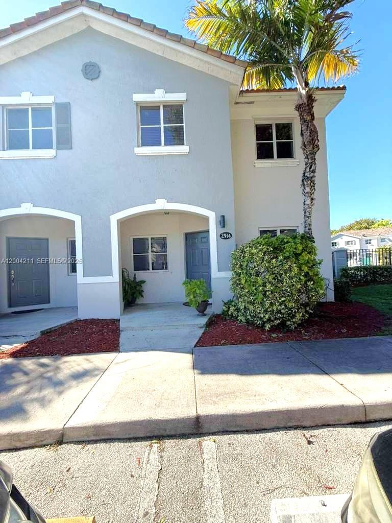 A two-story townhouse exterior features light gray stucco, arched entryways, and a palm tree — 2914 SE 15th Ter, Homestead FL 33035, HOMESTEAD, FL