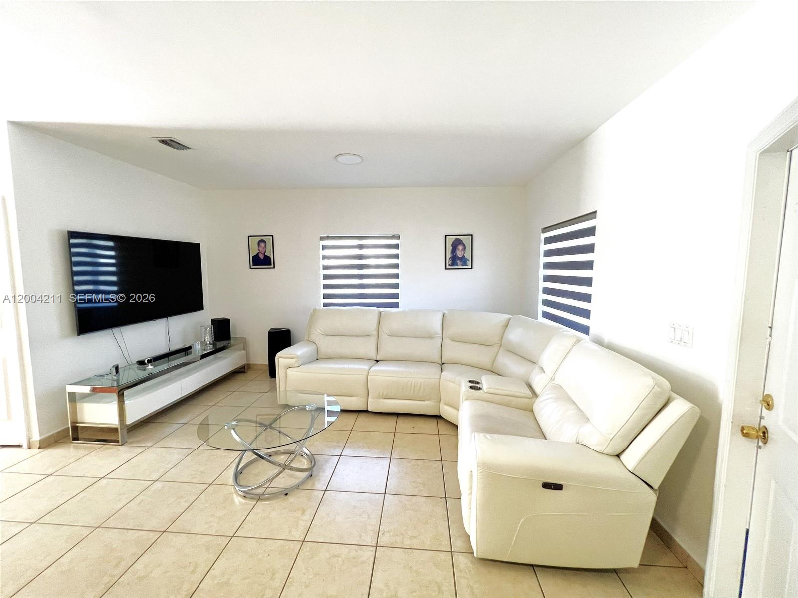 A living room features a white sectional sofa, a glass coffee table, and a wall-mounted television — 2914 SE 15th Ter, Homestead FL 33035, HOMESTEAD, FL