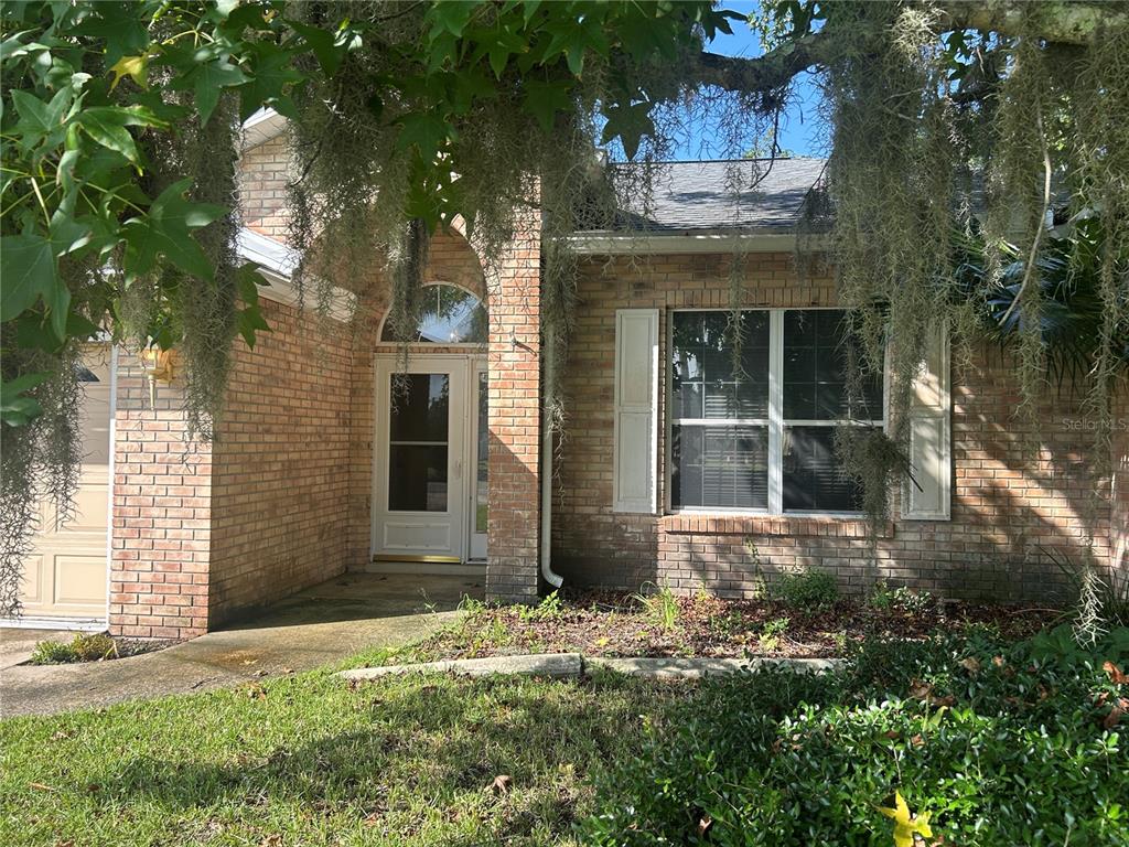A brick house exterior features a front entrance, a garage, and hanging Spanish moss — 5 BIRD HAVEN PLACE, PALM COAST, FL