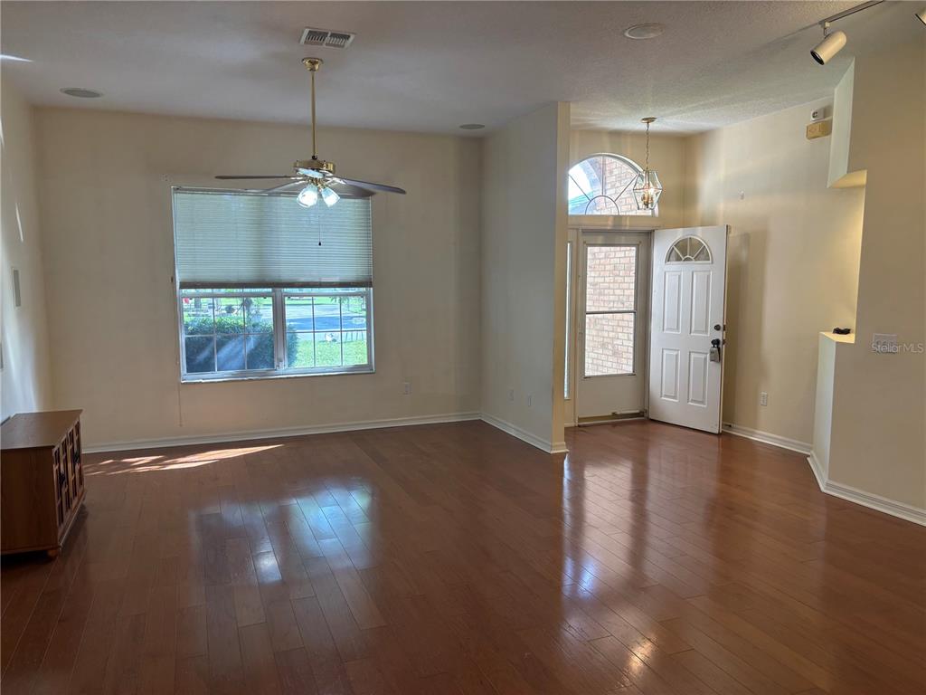 An empty living room features hardwood floors, a ceiling fan, and an open front door — 5 BIRD HAVEN PLACE, PALM COAST, FL