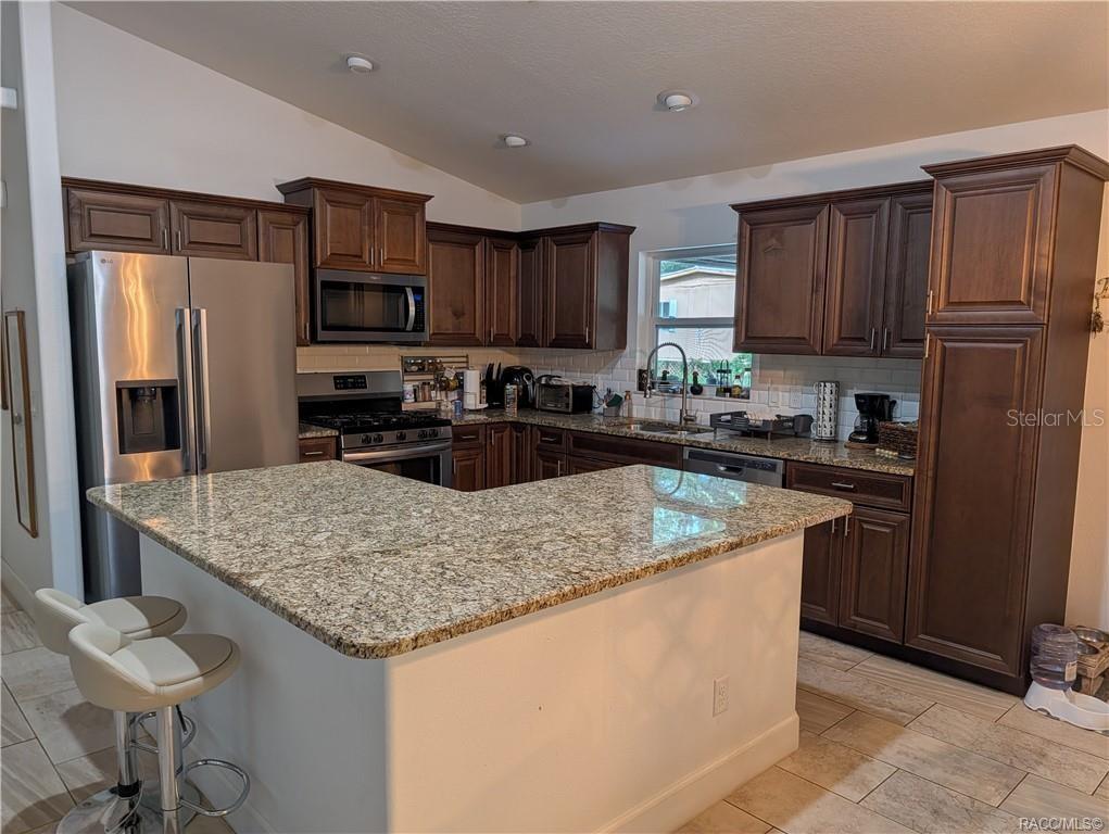 A kitchen features dark wood cabinets, granite countertops, stainless steel appliances, and a central island — 9711 S BERKSHIRE AVENUE, INVERNESS, FL