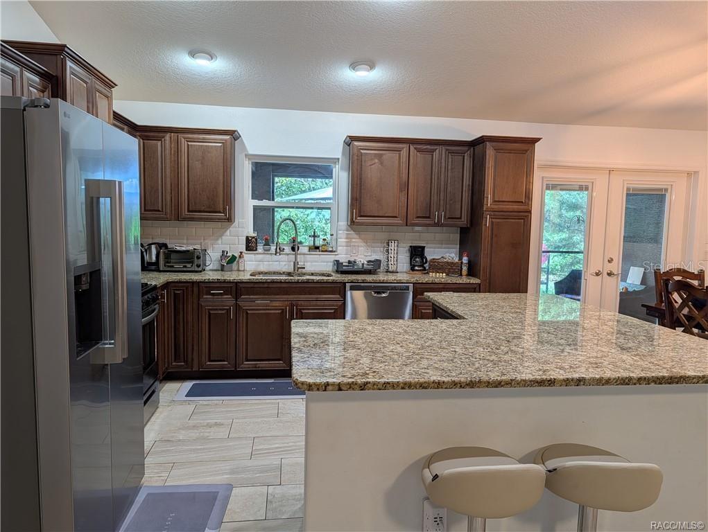 A kitchen features dark wood cabinets, granite countertops, stainless steel appliances, and a breakfast bar — 9711 S BERKSHIRE AVENUE, INVERNESS, FL