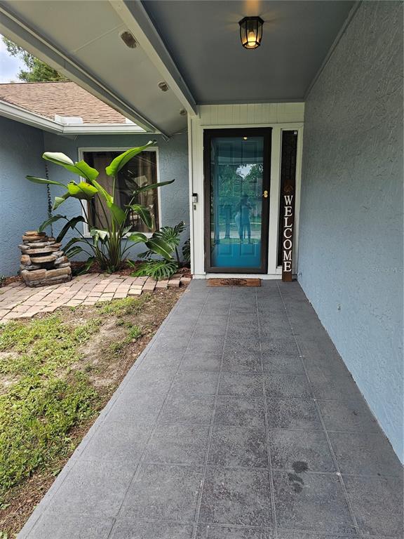 A covered entryway features a blue front door, a welcome sign, and a stone fountain — 18322 SWAN LAKE DRIVE, LUTZ, FL