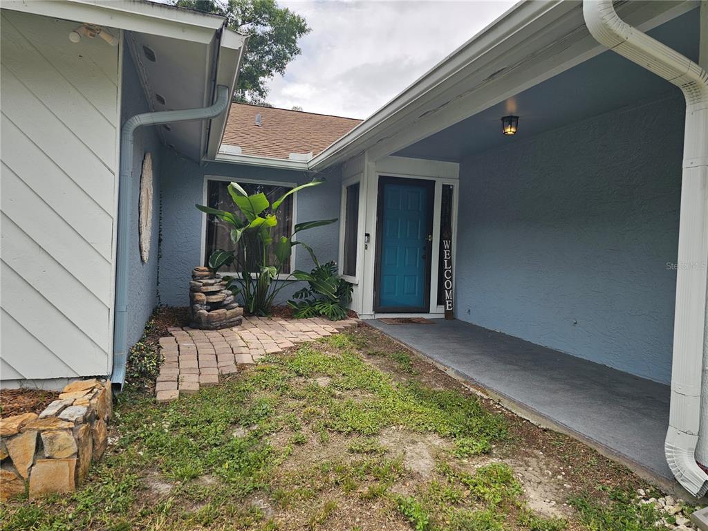 A blue house exterior features a covered entryway, a teal front door, and a stone fountain — 18322 SWAN LAKE DRIVE, LUTZ, FL