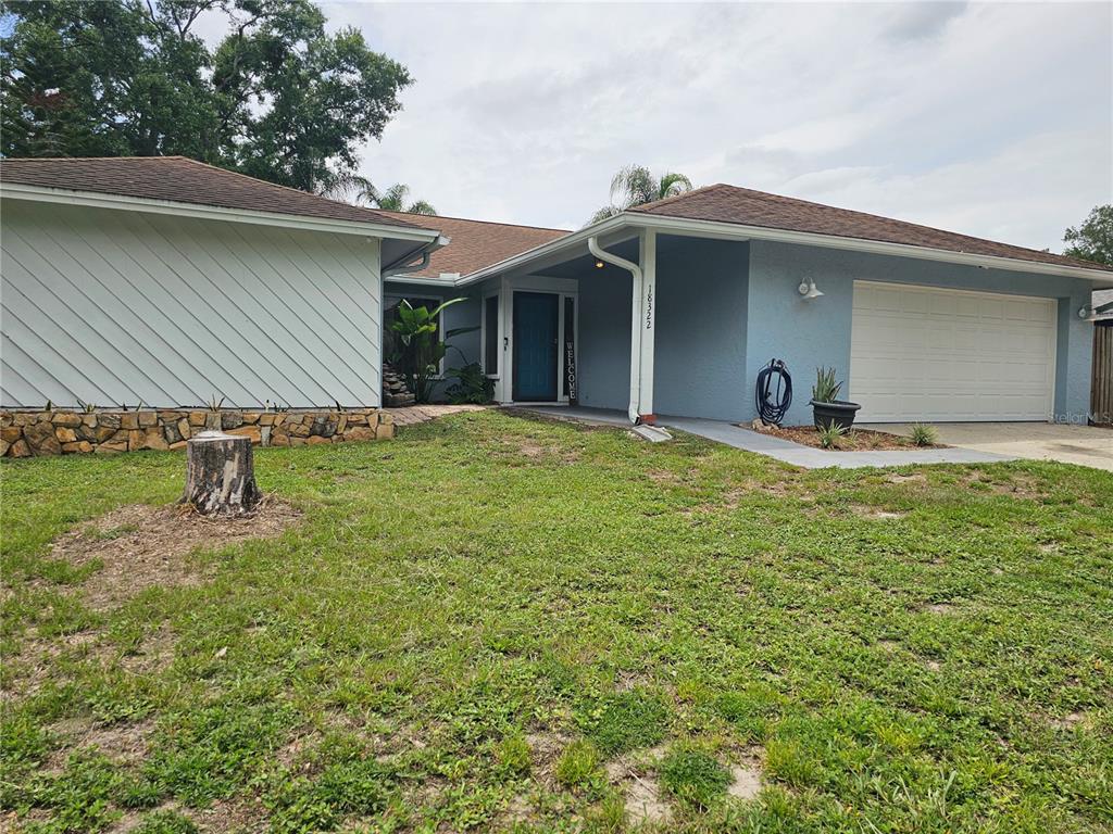 A single-story house with a blue exterior, a two-car garage, and a stone-accented front wall — 18322 SWAN LAKE DRIVE, LUTZ, FL