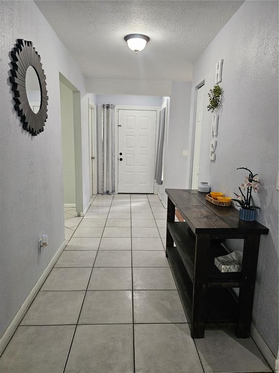 A tiled entryway features a dark wood console table, a sunburst mirror, and a white door — 18322 SWAN LAKE DRIVE, LUTZ, FL