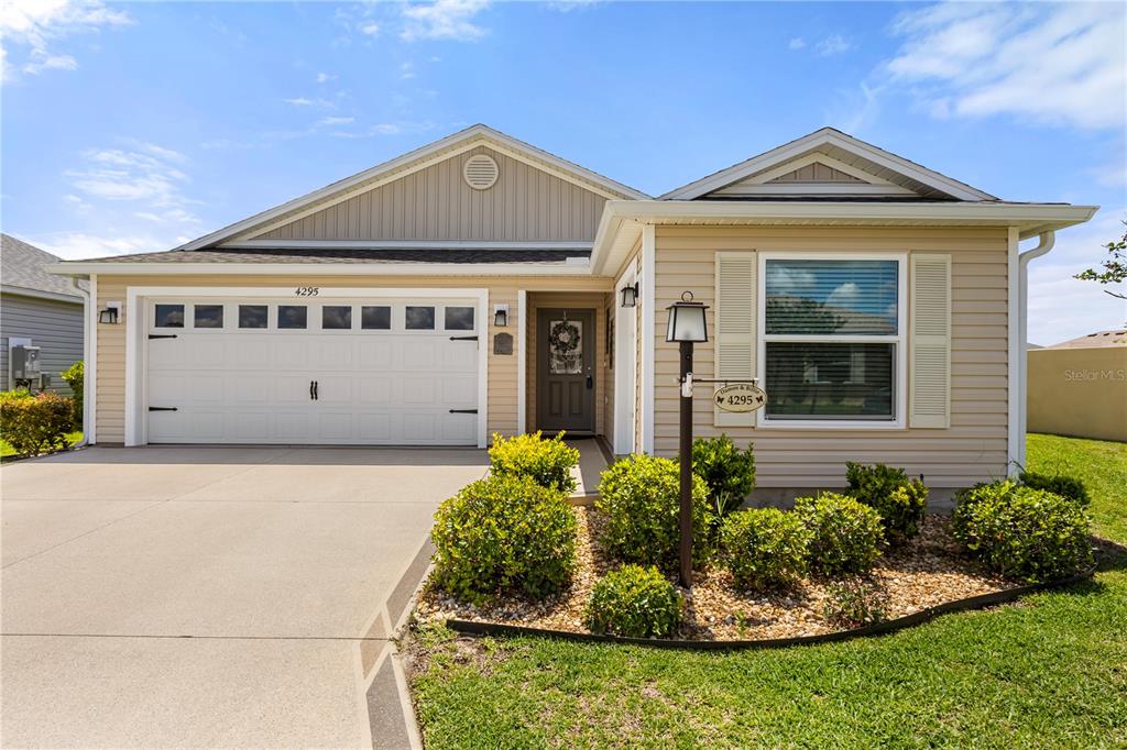 A single-story house with beige siding, a two-car garage, and a landscaped front yard — 4295 FREDDA TERRACE, THE VILLAGES, FL