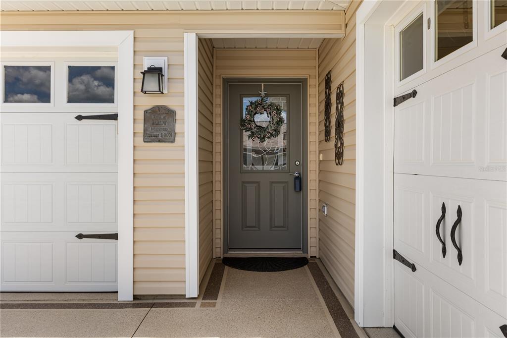 A gray front door with a wreath sits between two white garage doors — 4295 FREDDA TERRACE, THE VILLAGES, FL