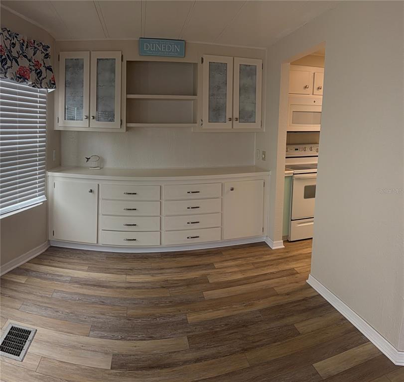 A dining room features white built-in cabinetry, wood-look flooring, and a view into the kitchen — 3301 ALT 19 UNIT 162, DUNEDIN, FL