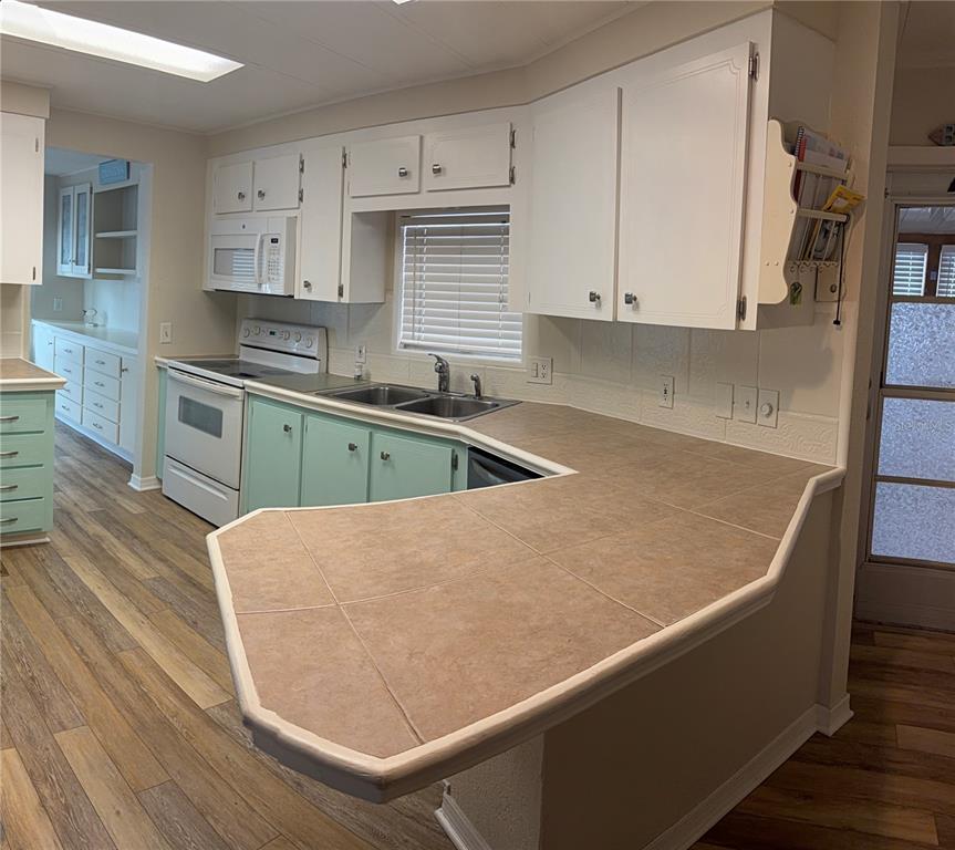 A kitchen features white upper cabinets, light green lower cabinets, and a tiled peninsula countertop — 3301 ALT 19 UNIT 162, DUNEDIN, FL