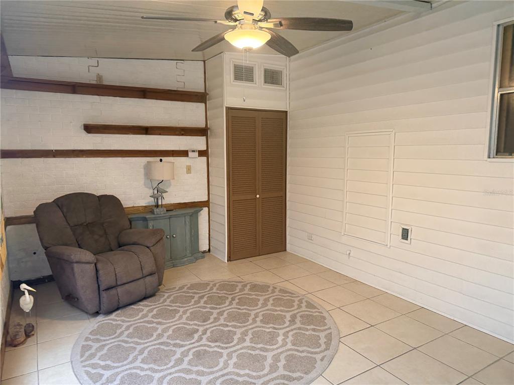A sunroom features tiled floors, a ceiling fan, a recliner, and a white brick wall — 3301 ALT 19 UNIT 162, DUNEDIN, FL