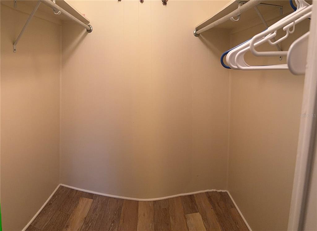 A walk-in closet features beige walls, wood-look flooring, and white wire shelving with hangers — 3301 ALT 19 UNIT 162, DUNEDIN, FL