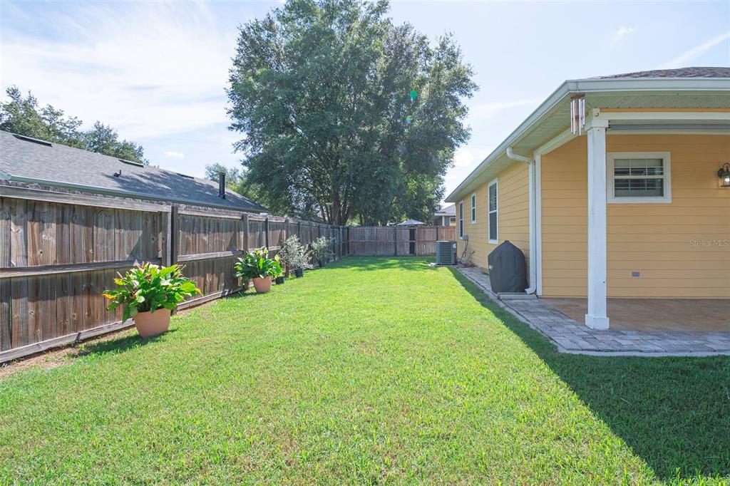 A grassy backyard features a wooden privacy fence, a covered patio, and potted plants — 14274 NW 9TH ROAD, NEWBERRY, FL