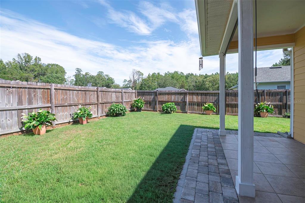 A backyard with a paved patio, a wooden fence, and several potted plants on grass — 14274 NW 9TH ROAD, NEWBERRY, FL