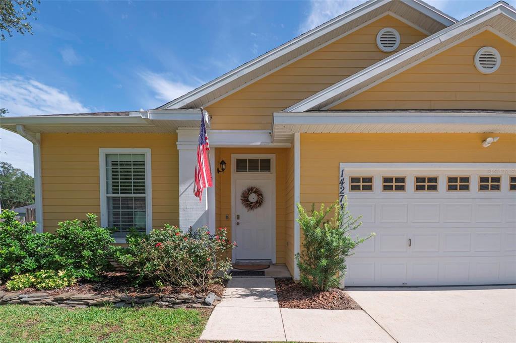 A yellow single-story house features a white garage door, a front porch, and a flag — 14274 NW 9TH ROAD, NEWBERRY, FL