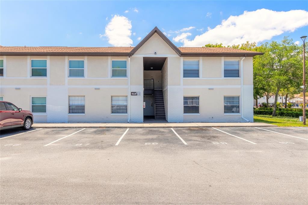 A two-story apartment building exterior features a central staircase and a paved parking lot — 415 BANANA CAY DRIVE UNIT F, SOUTH DAYTONA, FL