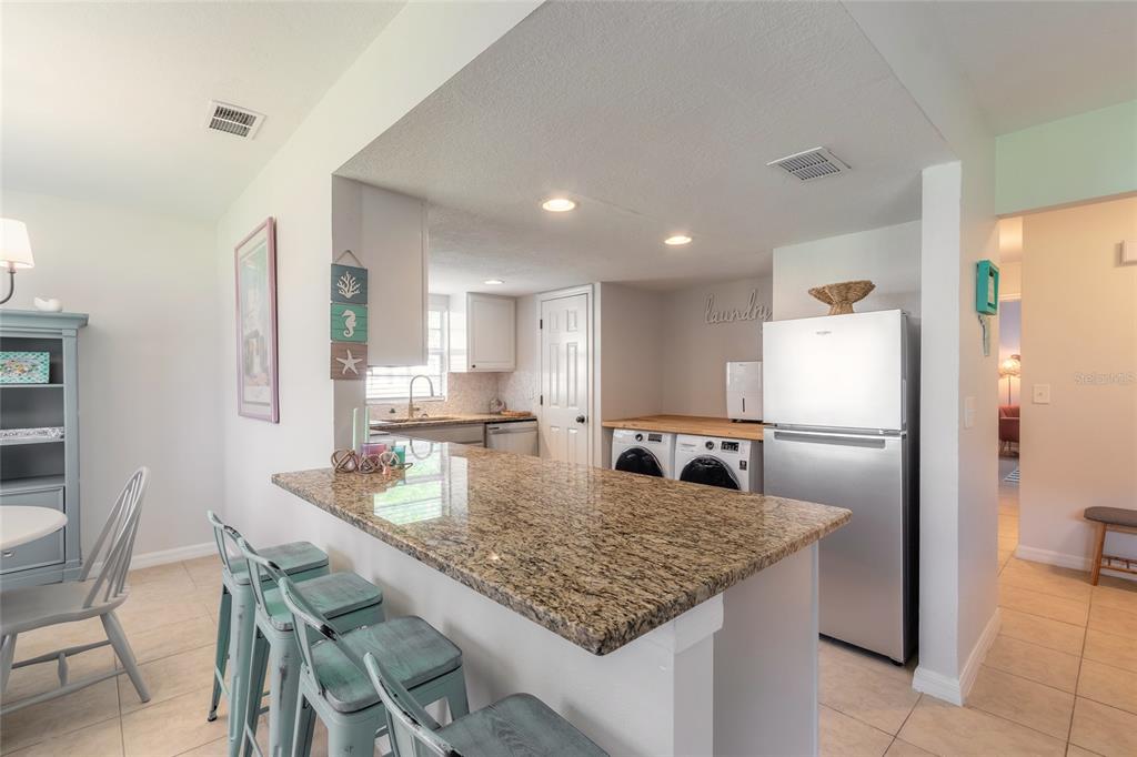 A kitchen features a granite-topped island, stainless steel refrigerator, and an adjacent laundry area — 415 BANANA CAY DRIVE UNIT F, SOUTH DAYTONA, FL