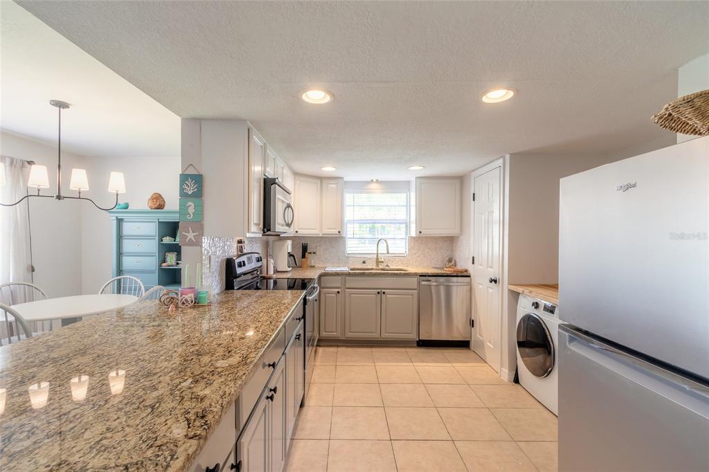 A kitchen features granite countertops, white and gray cabinetry, stainless steel appliances, and tile flooring — 415 BANANA CAY DRIVE UNIT F, SOUTH DAYTONA, FL