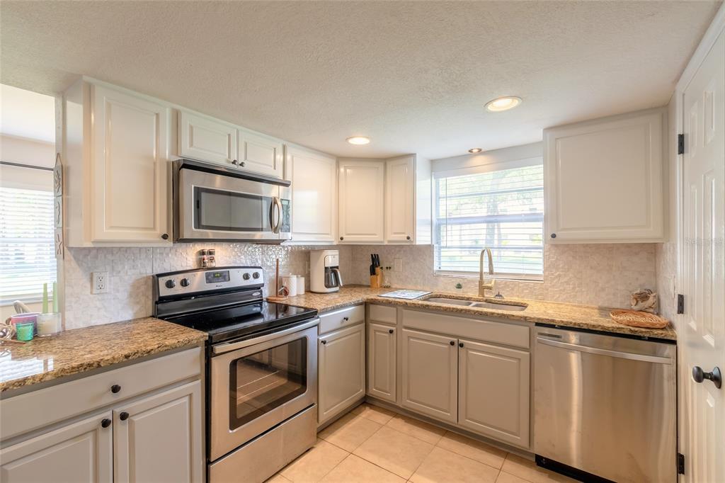 A kitchen features white upper cabinets, light gray lower cabinets, granite countertops, and stainless appliances — 415 BANANA CAY DRIVE UNIT F, SOUTH DAYTONA, FL
