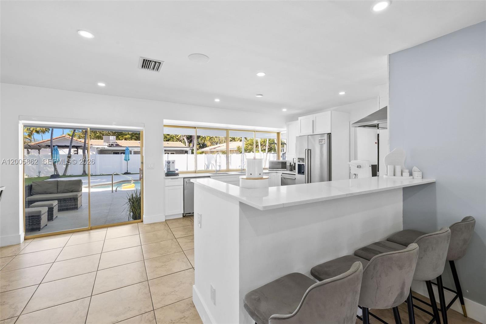 A white kitchen features a breakfast bar, stainless steel appliances, and sliding glass patio doors — 3460 N 46th Ave, Hollywood FL 33021, HOLLYWOOD, FL