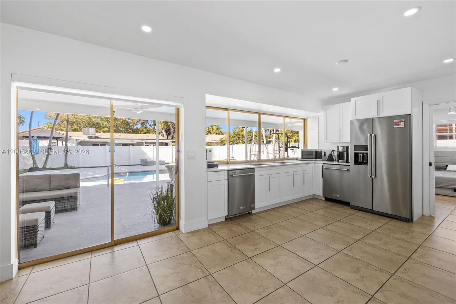 A kitchen with white cabinets, stainless steel appliances, and tile flooring overlooks a backyard pool — 3460 N 46th Ave, Hollywood FL 33021, HOLLYWOOD, FL
