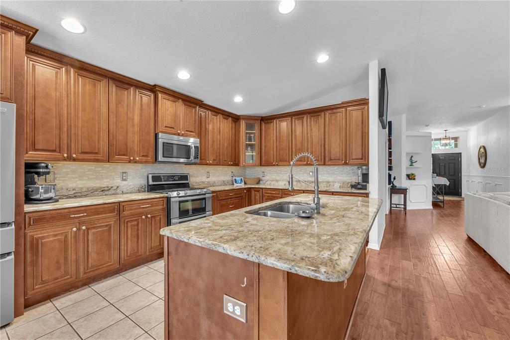 A kitchen features wood cabinets, granite countertops, a central island, and tile flooring — 16316 BRIDGEGLADE LANE, LITHIA, FL