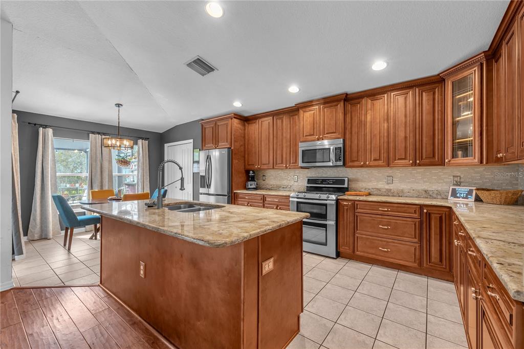 A kitchen features wood cabinets, granite countertops, a center island, and stainless steel appliances — 16316 BRIDGEGLADE LANE, LITHIA, FL