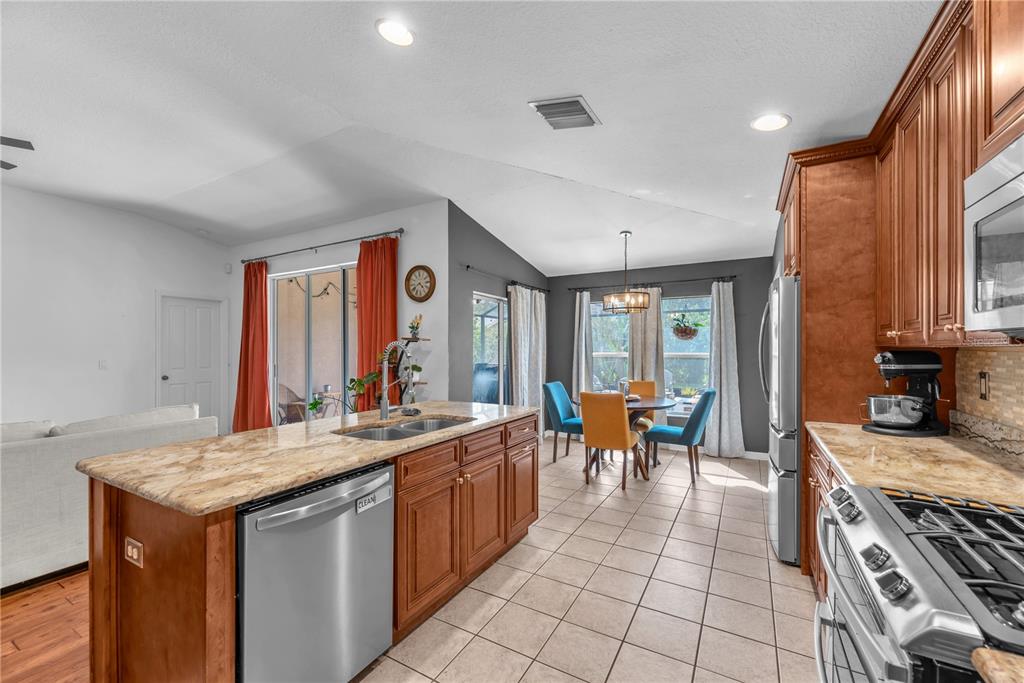 A kitchen with wood cabinets, granite countertops, a stainless steel dishwasher, and a dining area — 16316 BRIDGEGLADE LANE, LITHIA, FL