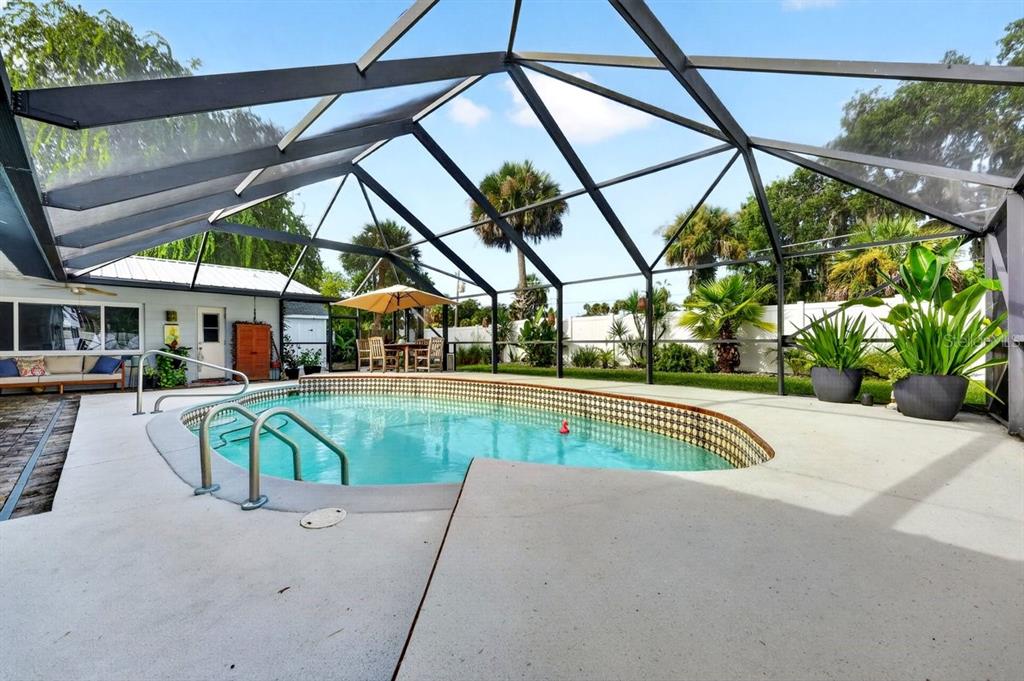 A screened-in pool area with a patio, outdoor dining set, and tropical landscaping — 237 BRITTANY AVENUE, PORT ORANGE, FL